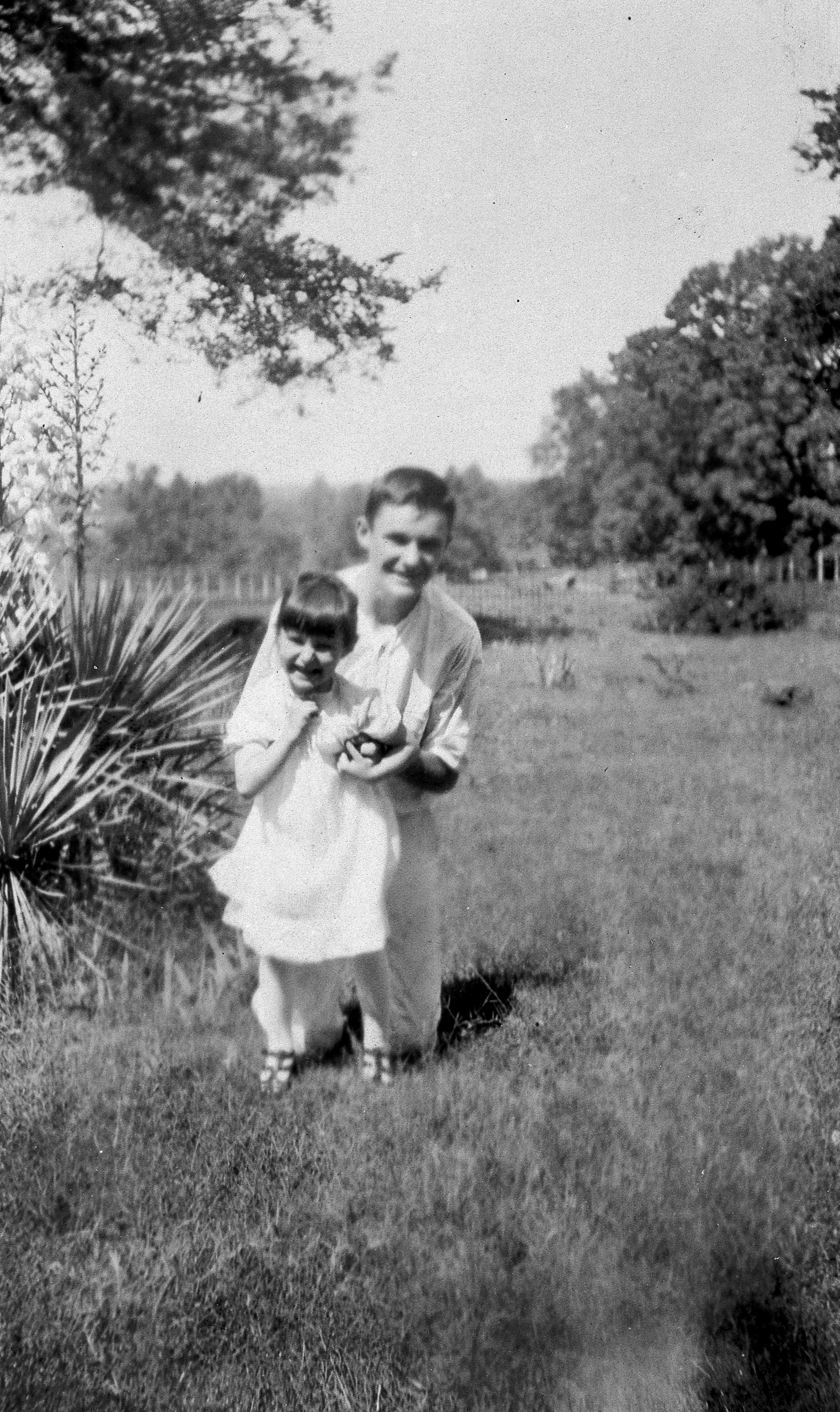 Lady Bird standing near a plant with spiky leaves, her brother kneeling behind her.